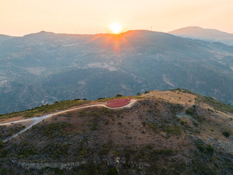 Aerial view of the Labirinto di Arianna sculpture on a hilltop during sunset with mountains and wind turbines in the background in Castel di Lucio, Sicily, Italy.