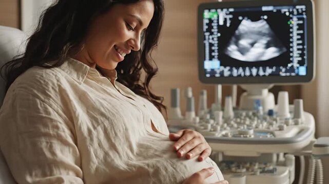 Smiling pregnant woman touching belly near ultrasound machine in clinic
