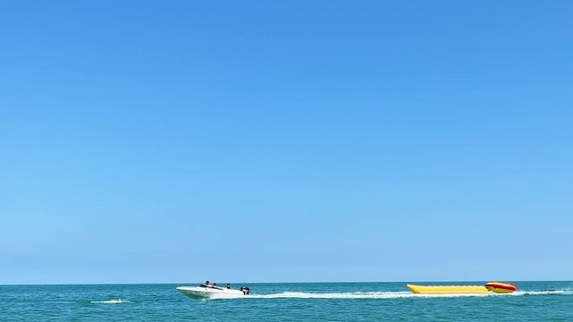 Travel sun day video. White launch rolls yellow banana boat on Black Sea. Blue sky, ocean wave. Concept of tubing, holiday, summer vacation, tourism, trip, swim, relax, rest, aqua sport. Copy space