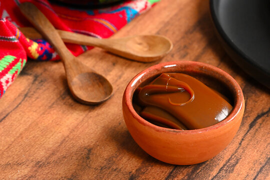 Mexican traditional cajeta of dulce de leche in a small clay pot with wooden spoon on a wooden background