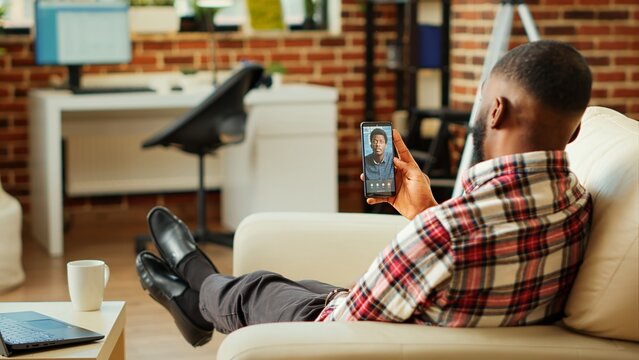 Man checking up on abroad living friend during video conference meeting over the internet. African american mates enjoying time together in online video call session while at home