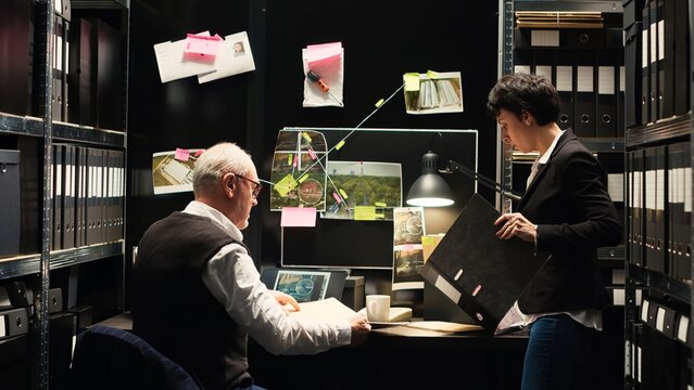 Police agents working together on case, evaluating forensic evidence and new clues in confidential records files. Detective and criminal expert reviewing witness testimony. Tripod shot.