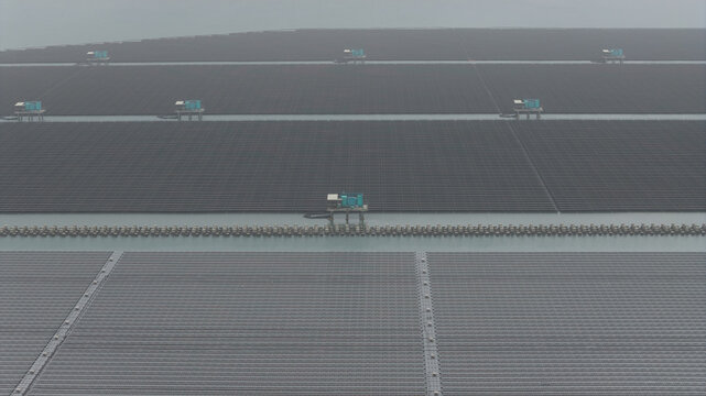 Aerial view of floating solar panels at the Changhua Coastal Industrial Park with blue utility platforms under a misty sky in Haipu Village, Changhua County, Taiwan.