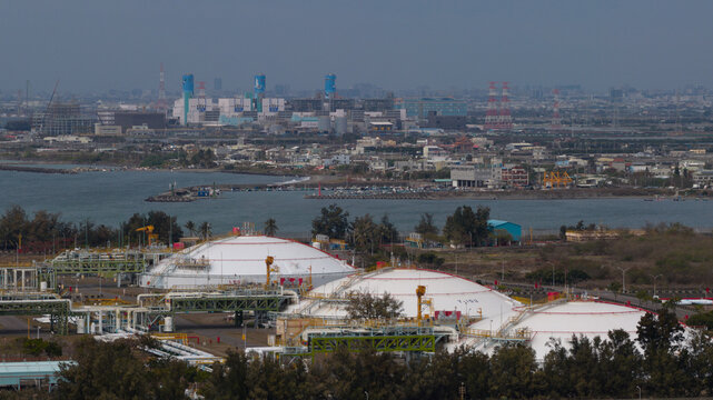 Aerial view of the East Wing LNG receiving station with large white storage tanks and industrial pipes near the coast in Yong'an District, Kaohsiung City, Taiwan.