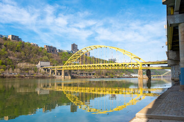 Fototapeta premium Fort Pitt Bridge Crosses Monongahela River in Pittsburgh With Clear Sky and Green Hillside in View During Daylight Hours