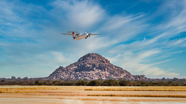 Twin-Engine Turboprop Passenger Plane Taking Off Over a Rocky Hill near an airfield runway