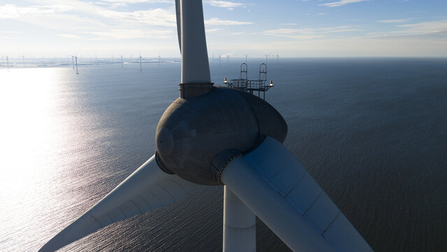 Aerial view of the nacelle and blades of a large wind turbine over the IJsselmeer with a field of turbines in the distance in Espel, Flevoland, Netherlands.