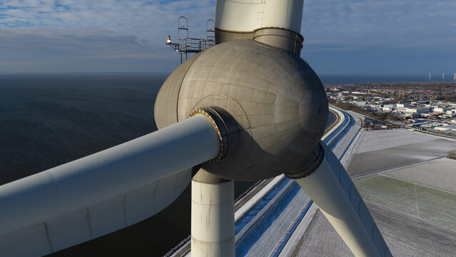 Aerial view of the massive nacelle and rotor hub of a wind turbine at Westermeerdijk overlooking the frozen coast and industrial area in Espel, Flevoland, Netherlands.