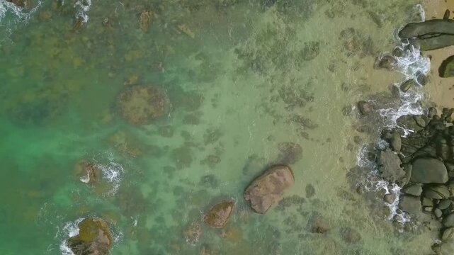 aerial view from above of giant ocean waves crashing and foaming on empty sand tropical beach with big rock stones