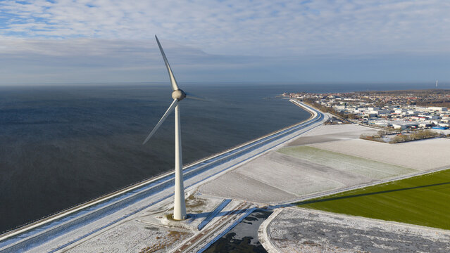 Aerial view of a large wind turbine standing on the Westermeerdijk dike next to the sea with frost-covered fields Espel, Flevoland, Netherlands.