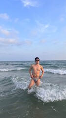 Fototapeta premium Handsome male model in swimwear playing in the ocean at sunset beach, Thailand.