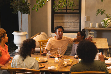 Diverse friends listening, Asian man wearing beige tee gesturing at wooden table with candles © wavebreak3