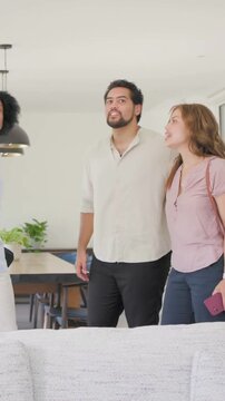 Vertical video: Arriving couple shaking hands with host in blue, touring modern home noting windows