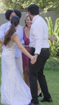 Vertical video: Stepping in friends congratulating and hugging newlyweds on lawn, with gown and tie