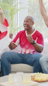 Vertical video: Cheering fan in red jersey pumping fists, clapping at home after goal, with drinks