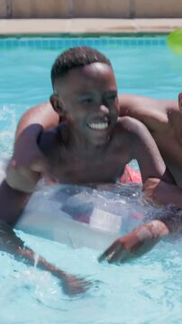Vertical video: Leaning son, dad holding and splashing on float in home pool for fun in trunks