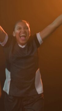Cheering in studio, woman in black-white jersey waving tricolor flag, hugging teammate celebrating