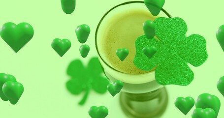 Fototapeta premium Drifting glossy green hearts circling stemmed glass holding frothy drink in studio, glitter clover