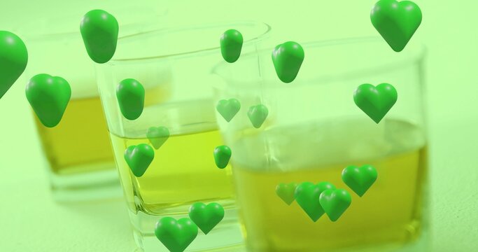Animating green hearts floating around two clear glasses with yellow liquid on pale green surface