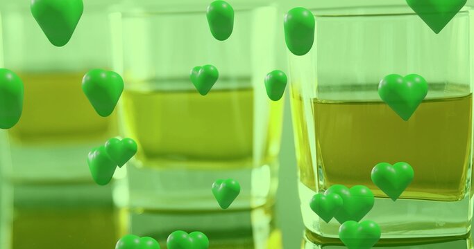 Showing square glass tumbler on reflective table, holding amber liquid and green hearts, copy space