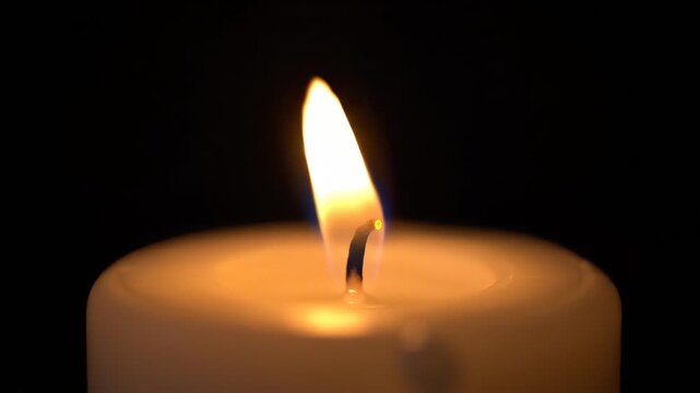 Single candle flame burning against a black background macro shot