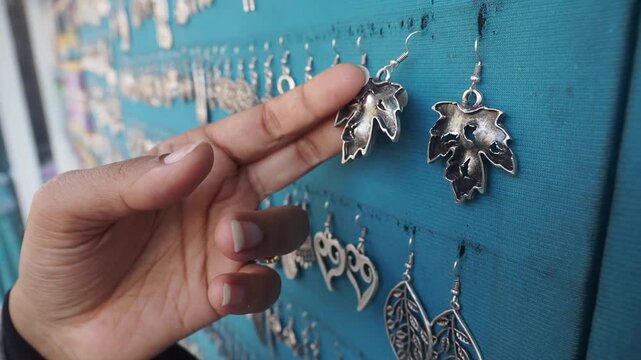 Woman hands touching silver leaf earrings display at jewelry shop market close up footage.