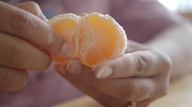 Close up hands peeling segments of fresh juicy mandarin orange fruit indoors on day light.