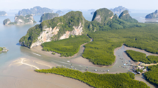 Aerial view of the limestone karsts and dense mangrove forests of Phang Nga Bay with small boats navigating the winding river in Thailand.