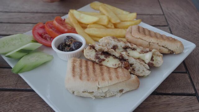 Gourmet grilled beef and cheese panini sandwich served with french fries and fresh veggies.