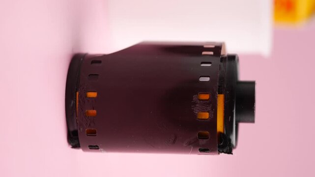 Close up of vintage 35mm film roll in canister against soft pink background.