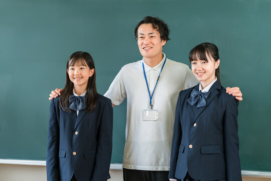 A male teacher and female elementary, middle, and high school students standing in front of the classroom blackboard.