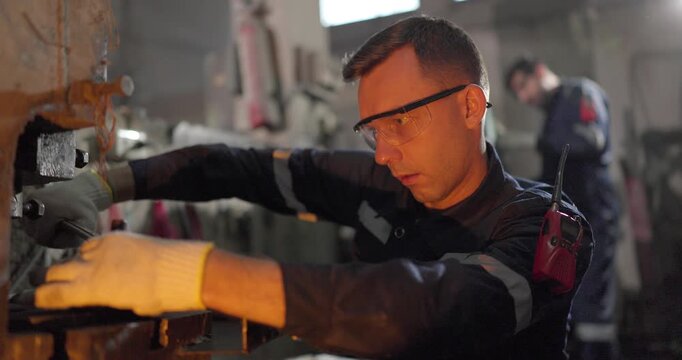 Factory technicians inspect heavy industrial machinery with flashlight, checklist, and manual controls inside a legacy metal workshop, showing maintenance, safety, and skilled diagnostics.
