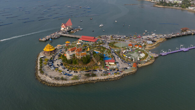 Aerial view of Ko Loi island featuring traditional Buddhist temples, a long pier, and a bridge connecting to the mainland with boats in the sea Chon Buri, Thailand.