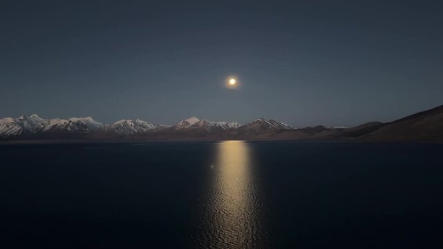 Captivating long time lapse showing the full process of the full moon setting and the subsequent golden sunrise light illuminating Kula Kangri peak over Puma Yumco Lake Tibet.