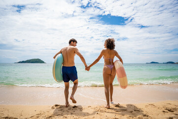 Fototapeta premium Rear view of a couple holding swimming inflatable and walk on the beach. 