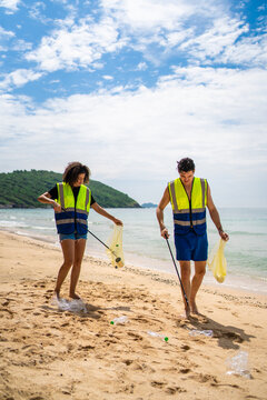 Two volunteers collecting plastic bottles and trash on a sandy beach. 