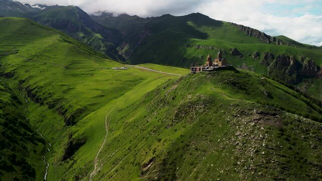 Cinematic 4K ProRes 422 aerial orbit of Gergeti Trinity Church at sunset. Iconic landmark in Kazbegi, Georgia, Caucasus.