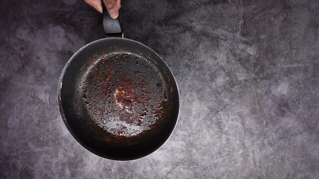 Dirty frying pan with burnt grease and food particles sits on dark gray stone background.