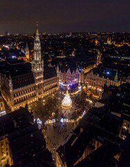 Fototapeta premium A nighttime aerial view of a city square filled with lights and buildings. A tall tower rises against a dark sky, with tiny figures