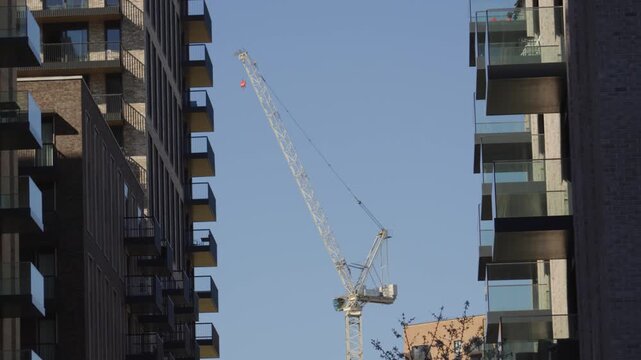 Huge Construction Tower Crane Between Apartment Buildings Constructing New Real Estate in London, UK. Minimalist urban skyline background representing city growth and future planning.