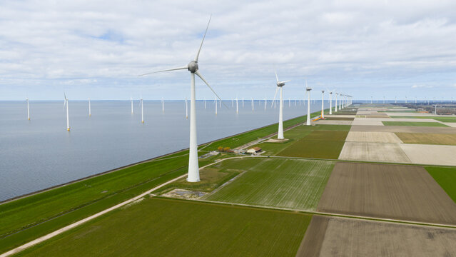 Aerial view of the Westermeerdijk wind turbines standing along the coastline and agricultural fields under a cloudy sky in Espel, Flevoland, Netherlands.
