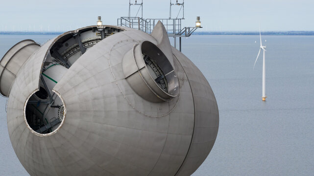Aerial view of the Westermeerdijk wind farm nacelle showing internal mechanical components with a distant turbine over the water in Espel, Flevoland, Netherlands.