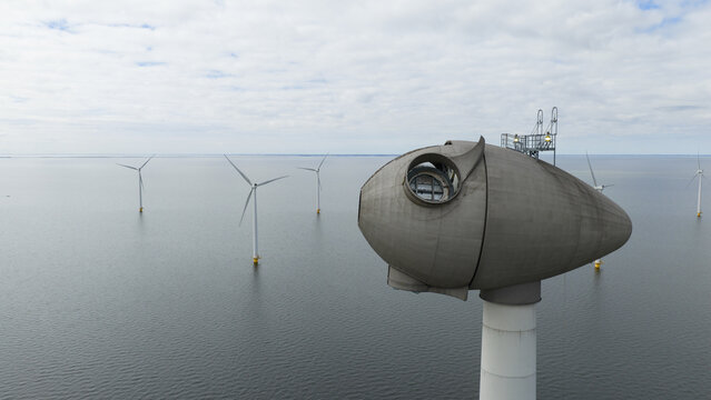Aerial view of a wind turbine nacelle at the Westermeerdijk wind farm with offshore turbines standing in the water under a cloudy sky in Espel, Flevoland, Netherlands.