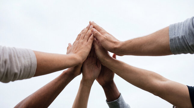 Diverse group of people showing unity and teamwork with hands stacked in a collective high-five gesture.