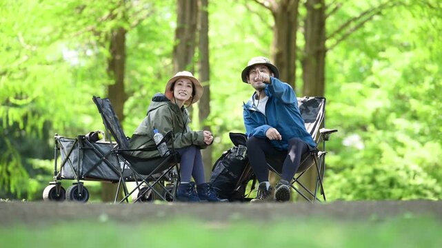 新緑のキャンプ場で椅子に座る笑顔のアウトドアやレジャーを楽しいミドルの夫婦　鳥や景色を眺める動画　指を差して見つめる