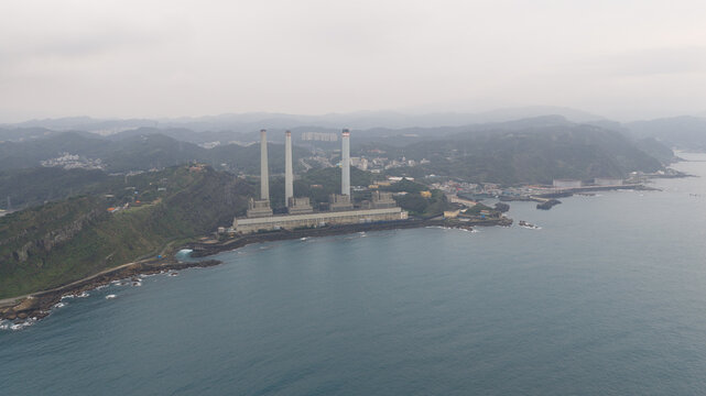 Aerial view of Concord Power Plant featuring three tall chimneys on the rocky coastline surrounded by lush green hills under an overcast sky in Xiehe Village, Keelung City, Taiwan.