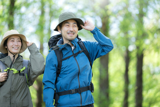 新緑の春の森の中を歩く夫婦のアウトドア、登山やトレッキングなどの運動イメージ上半身の笑顔のクローズアップ