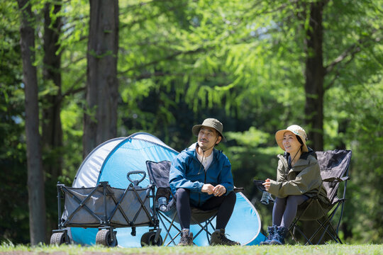 新緑のキャンプ場で椅子に座る笑顔のアウトドアやレジャーを楽しいミドルの夫婦　鳥や景色を眺める