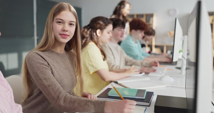 Students teenagers in classroom computers learning. Teens focus at screens as teacher supports, blending note taking and school tech practice for tasks. Clear concept of collaborative learning.