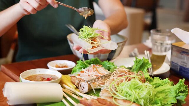 Person Adding Peanut Sauce to Vietnamese Spring Roll with Fresh Vegetables